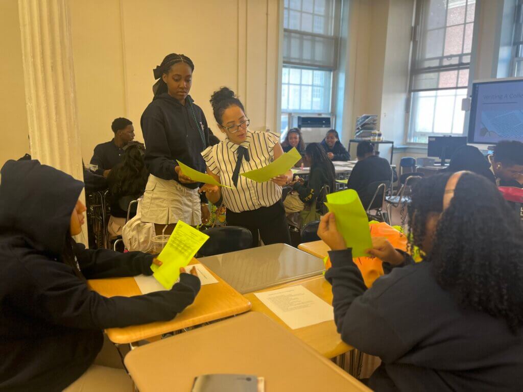 College counselor holds up two sheets of paper for comparison while student looks over her shoulder
