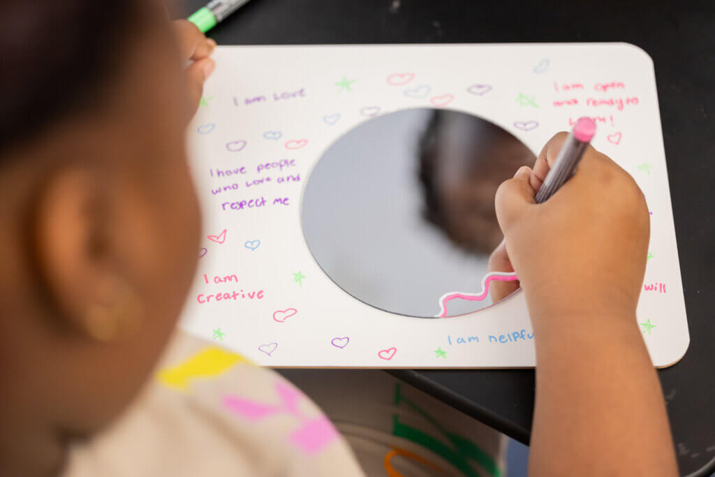 A student writes an empowering affirmation on a mirrored board