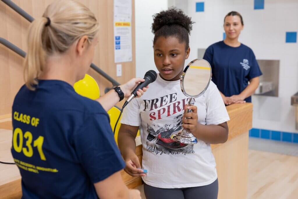 A student reciting an affirmation into a microphone while holding a mirror