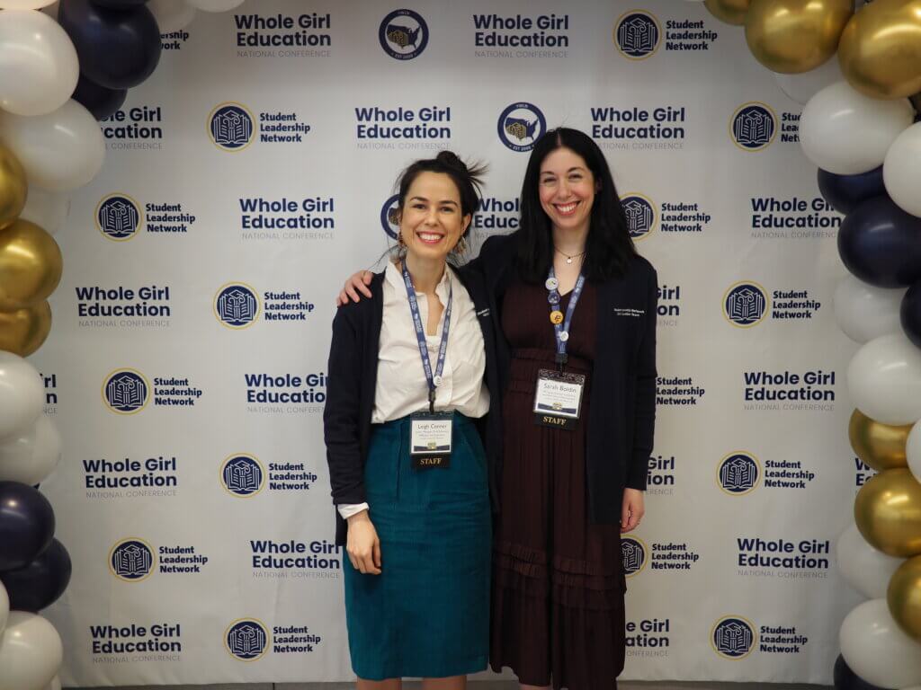 Two staff members pose for photo in front of backdrop at WholeGirl Education conference