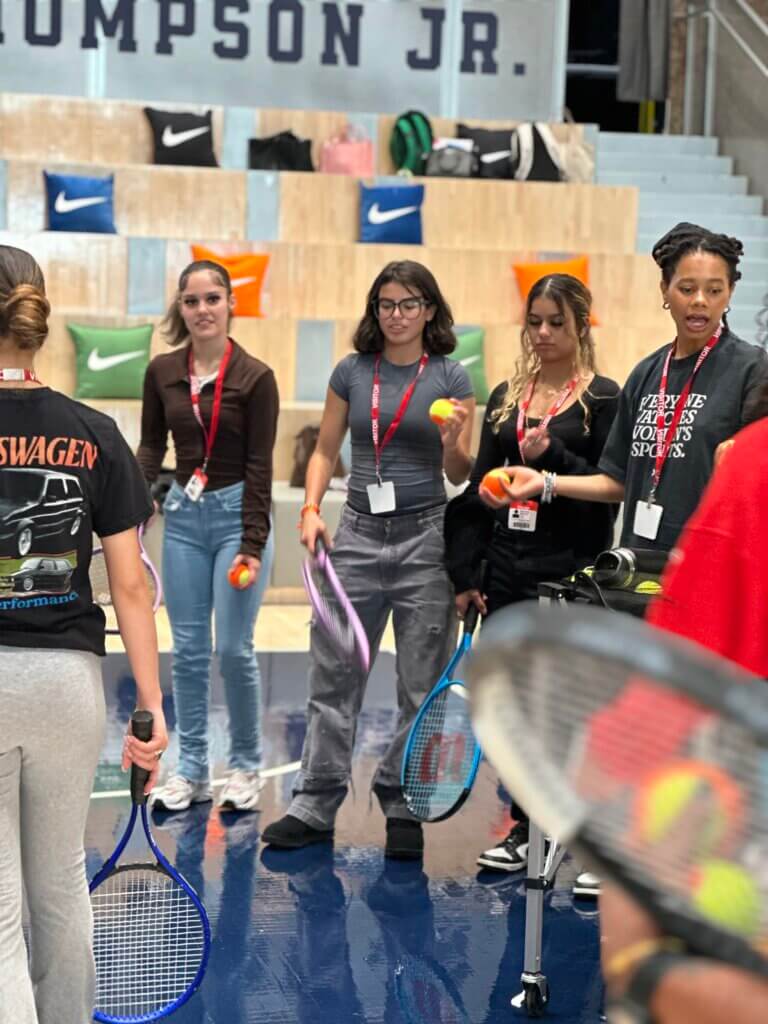 High school girls hold tennis rackets and tennis balls on a court