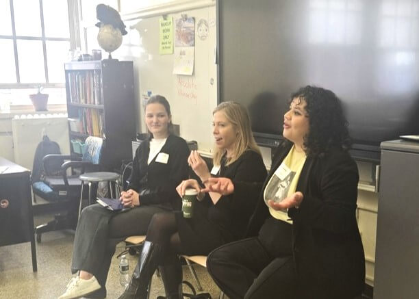 Three volunteers are seated in front of classroom, talking animatedly with their hands