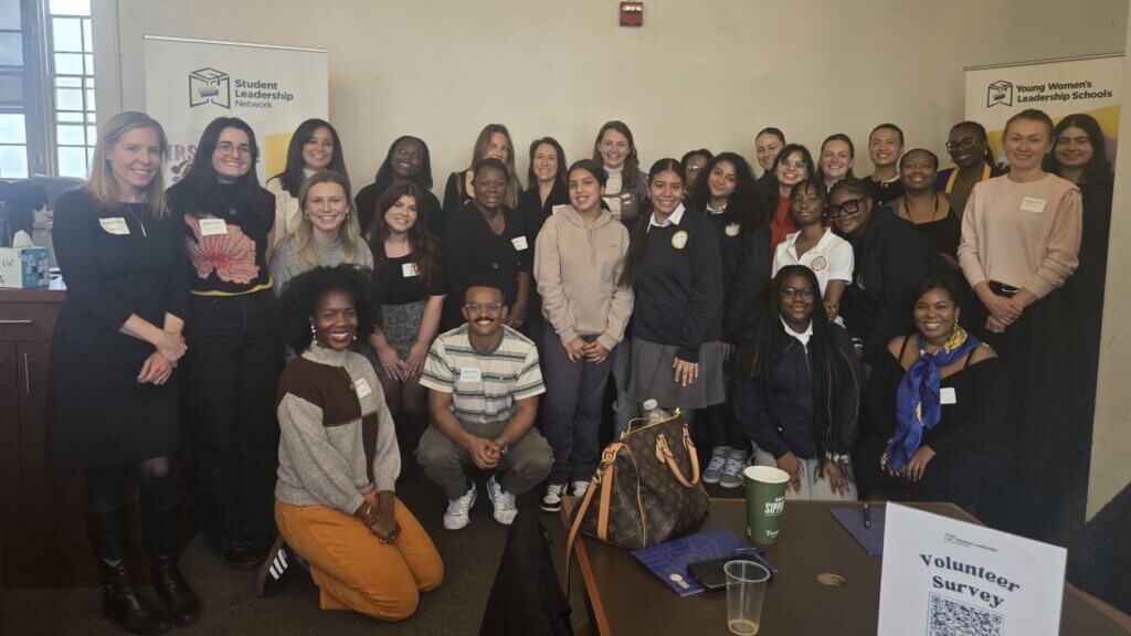 Group of students and volunteers pose for photo in a classroom