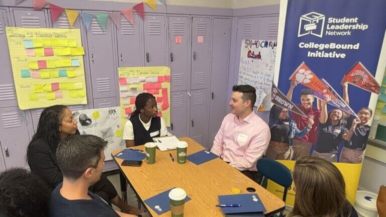 Group of volunteers and students are talking in a classroom by a wall of lockers