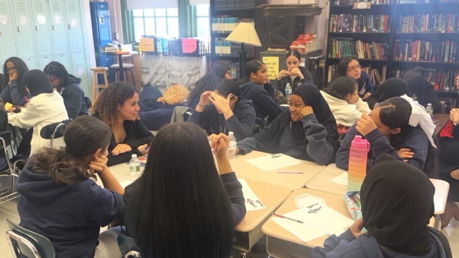 Group of students and volunteers are talking in a small circle in a classroom