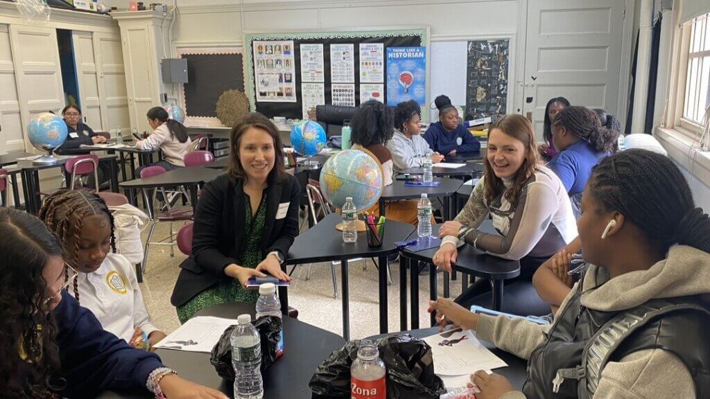 Group of students and volunteers are talking in a small circle in a classroom
