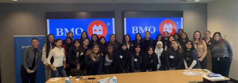 Students and BMO Capital employees pose for photo in front on conference room