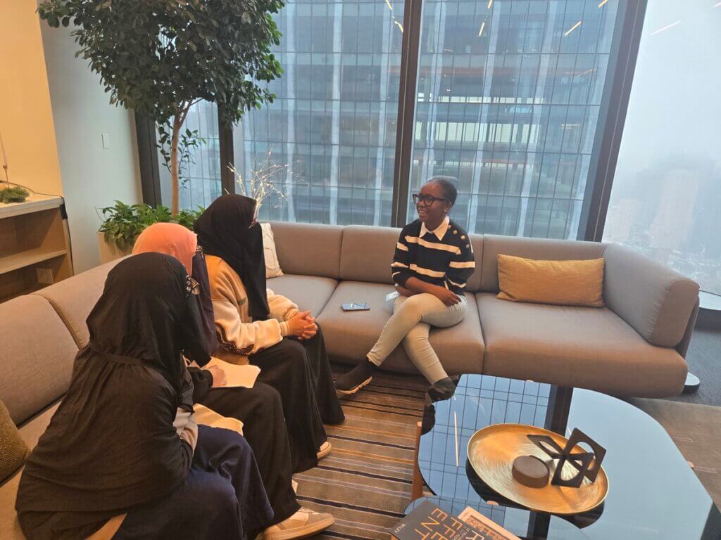 Adult volunteer and three students are talking with each other while seated on a couch