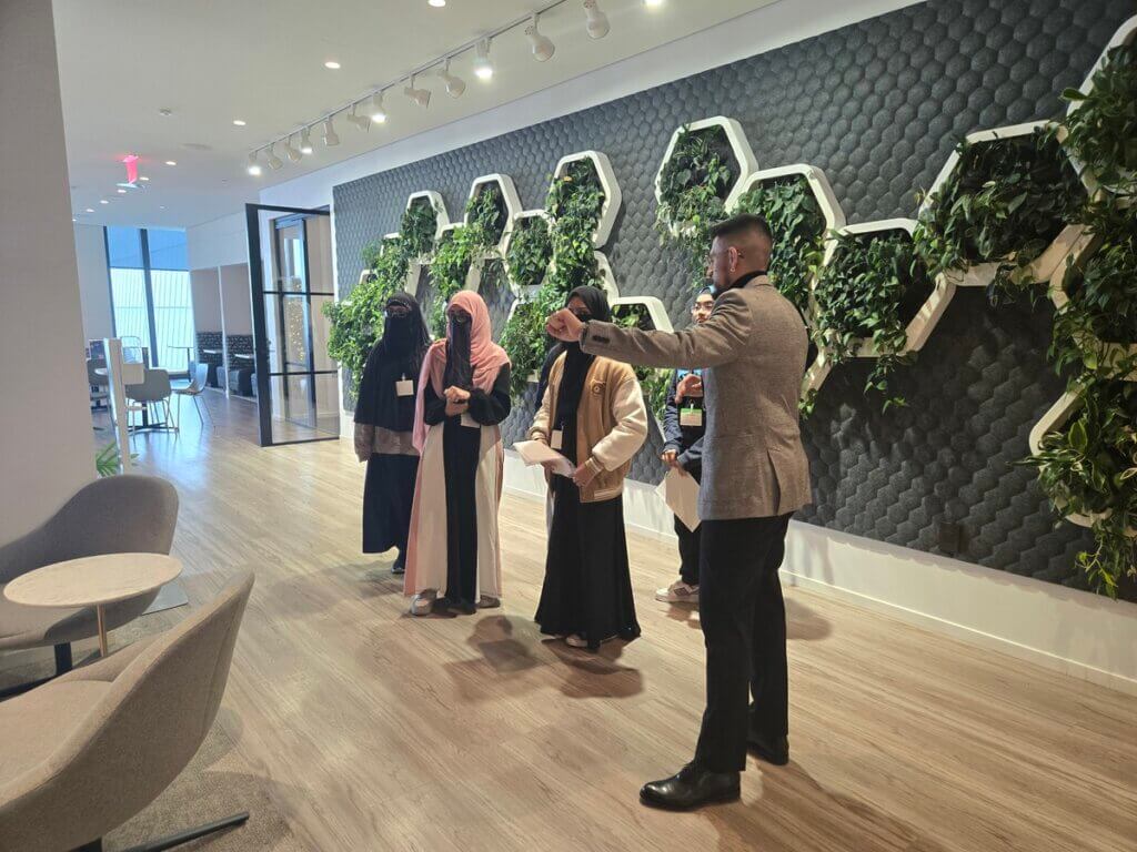 Employee leads tour of office for students, walking past a wall with live plants