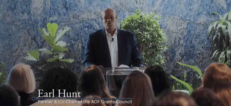 Male speaker in suit stands at podium, in front of a seated audience