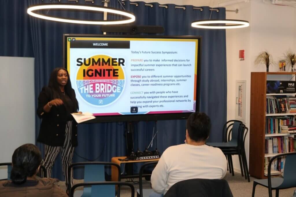 Nicole Meyer welcomes students at the front of the room, with the event agenda on a screen behind her.