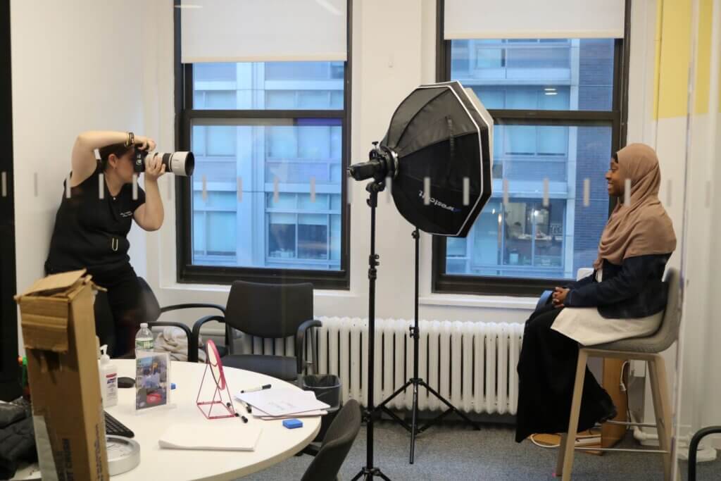 Photographer takes a headshot of student seated in front of camera lights