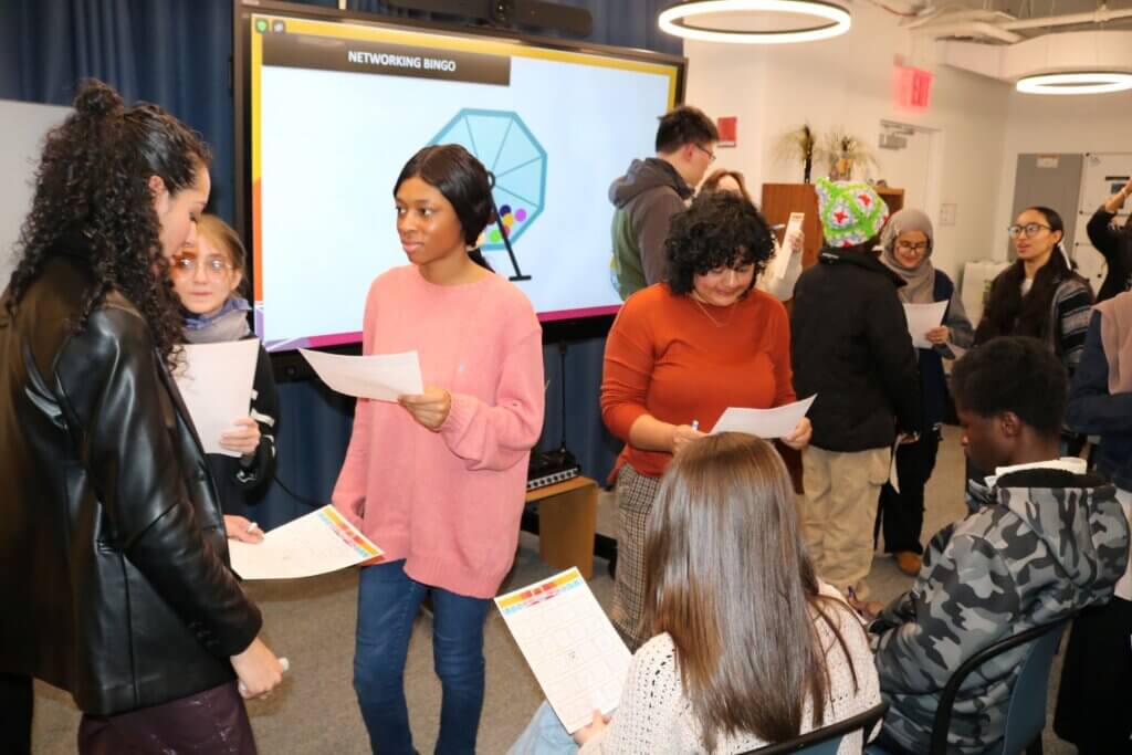 High school and college students hold up bingo sheets while talking with each other