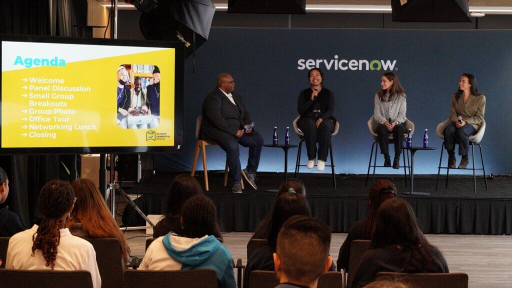 Four adults are seated on a stage, holding microphones, for a panel discussion