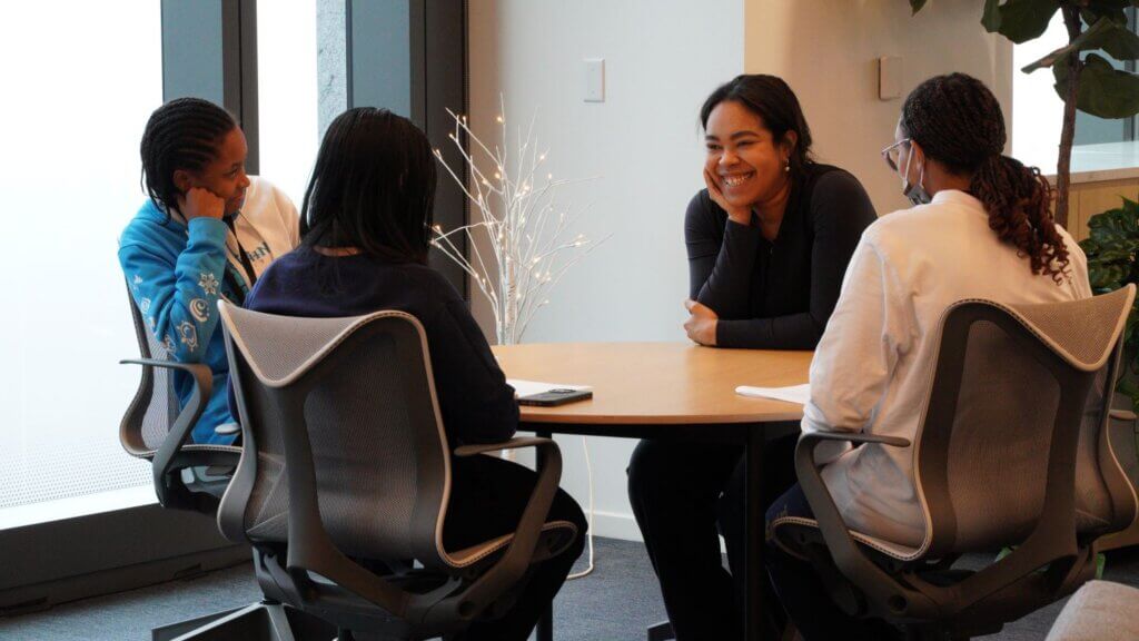 Adult volunteer and three students are talking with each other while seated at a table