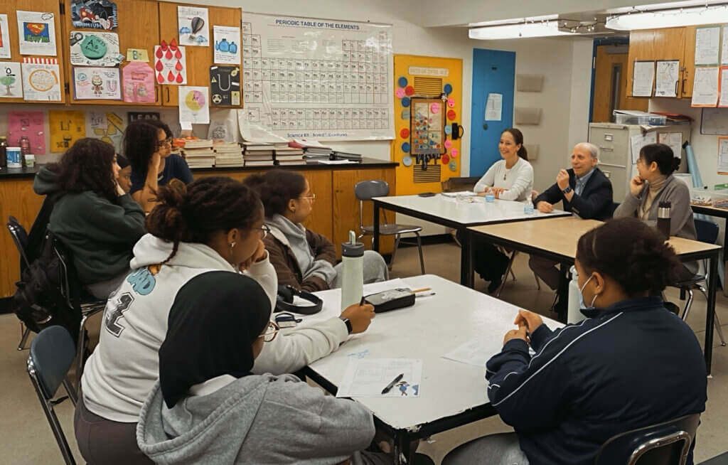 students listen to a panel of volunteers sitting at desks at the front of the classroom
