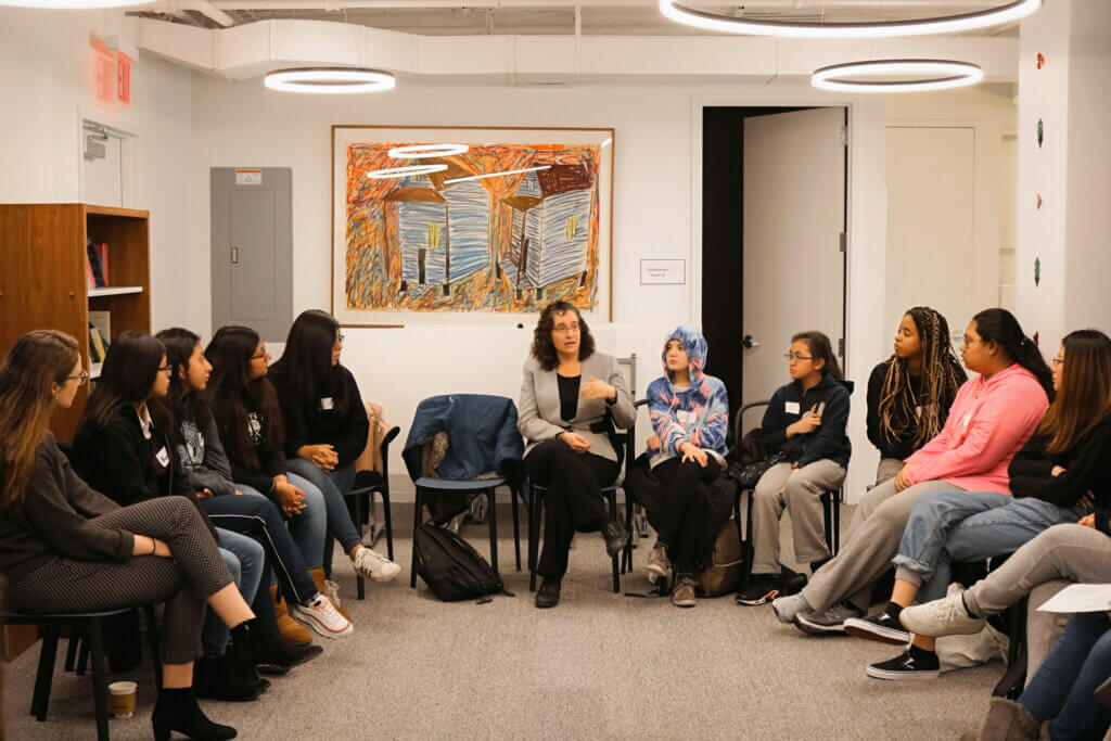 students sit in chairs in a U-formation listening to an adult sitting in the center seat
