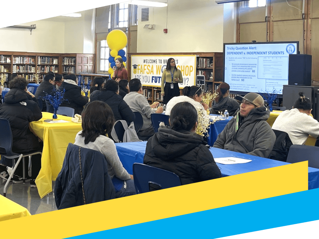 People sit at tables in a library while presenters lead a FAFSA workshop focused on college access. A screen displays information and decorations include balloons and yellow and blue tablecloths.