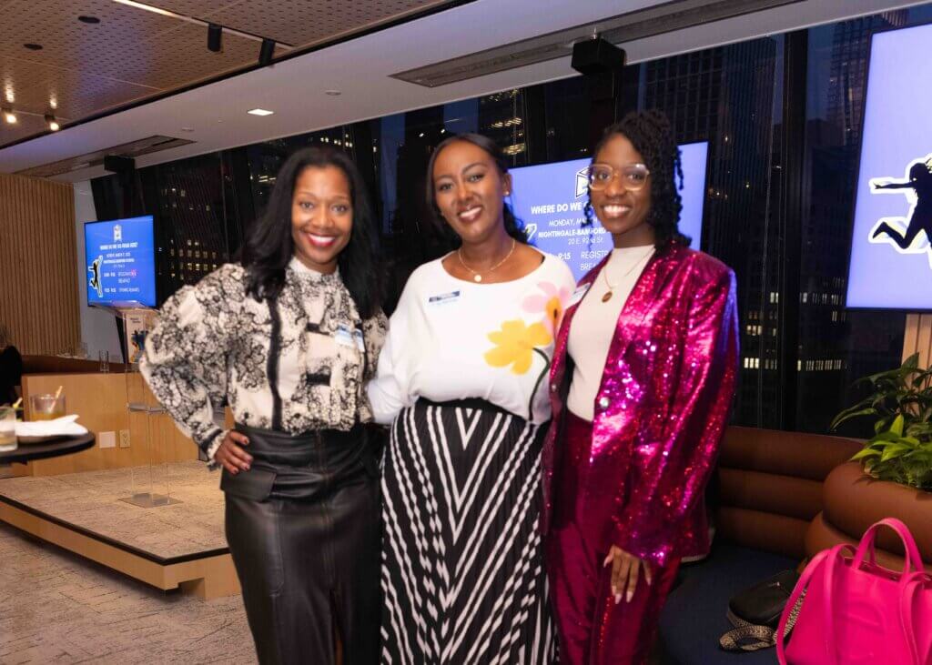 Three women in festive attire smile confidently at camera