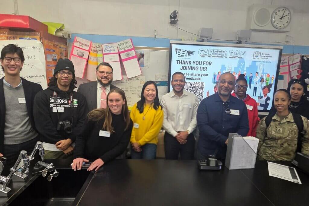 group of adult volunteers stand in front of classroom with "Career Day" on the screen behind them