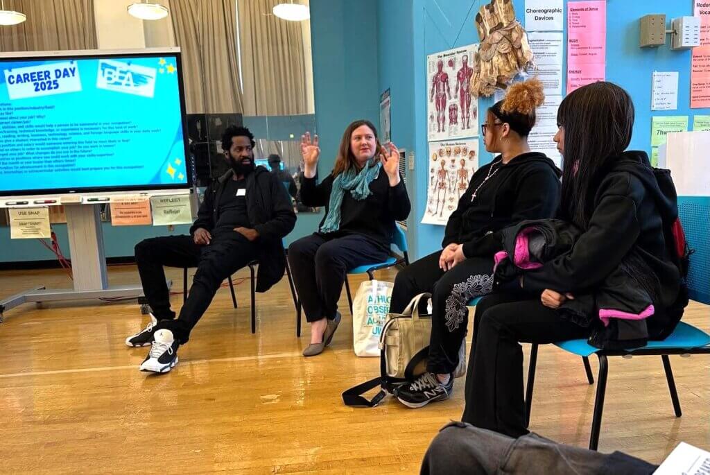 two adults and two students are seated talking with "Career Day" screen on left with questions to ask