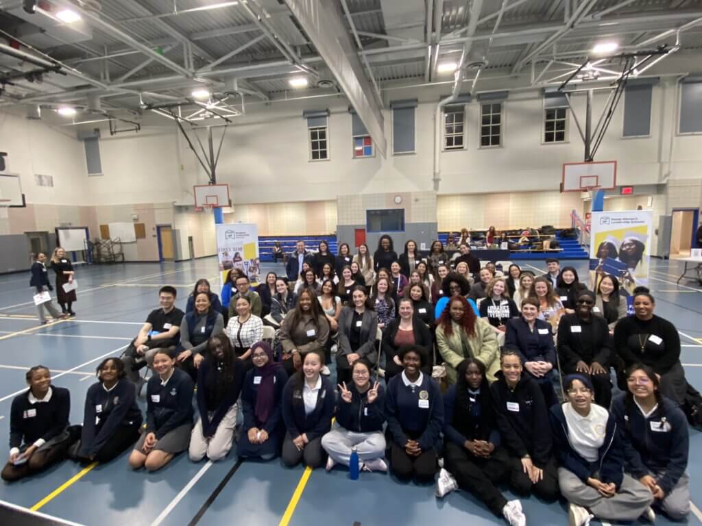 Group of 60 adult volunteers and students seated for photo in a school gymnasium