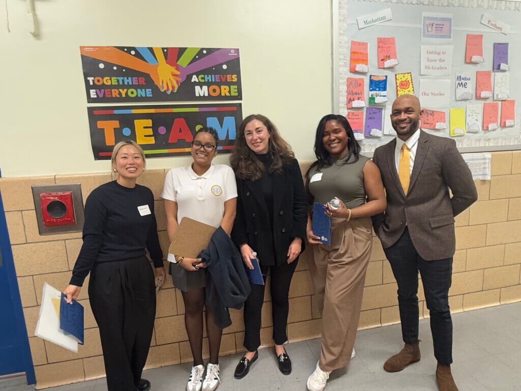 adult volunteers dressed in professional clothes with student who is wearing a school uniform pose for photo in hallway