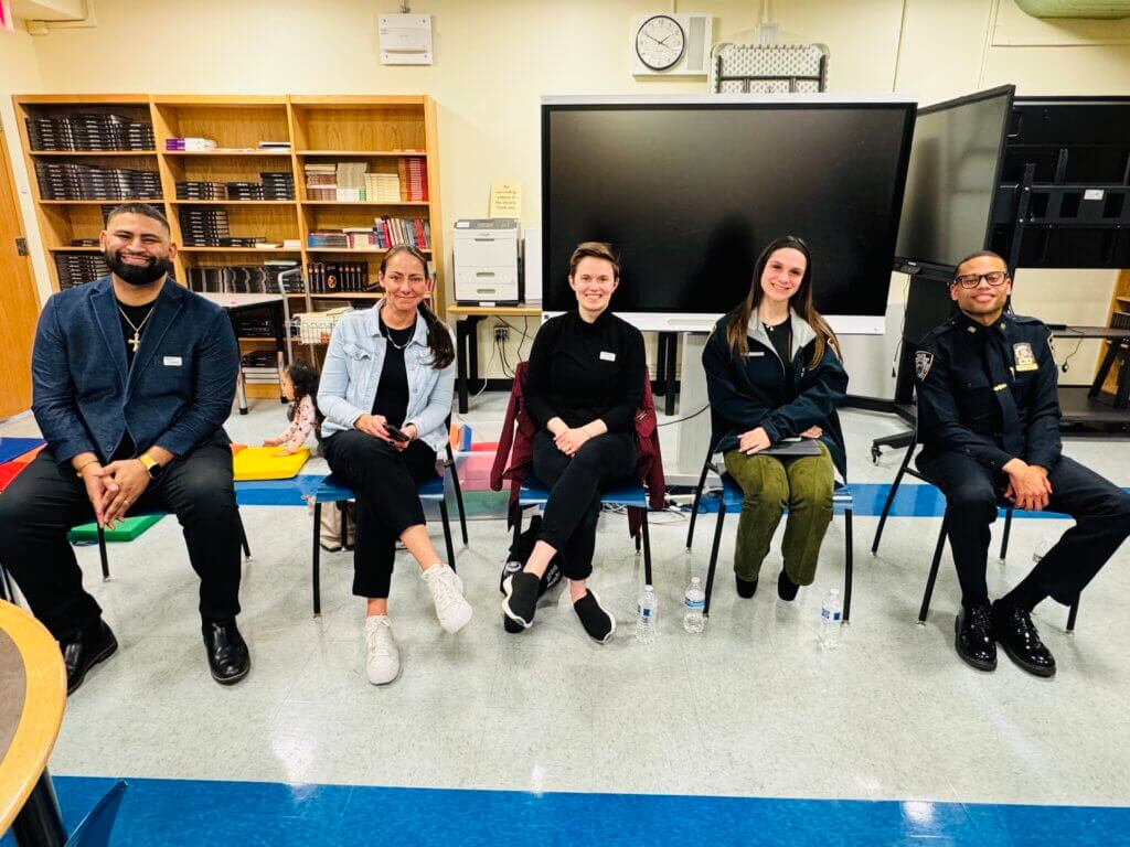 Five adult panelists seated in front of classroom