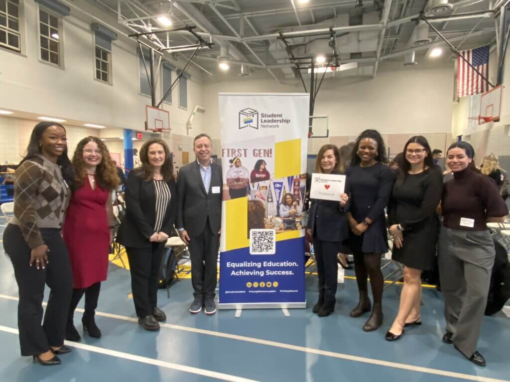 volunteers hold up Proskauer sign by Student Leadership Network banner