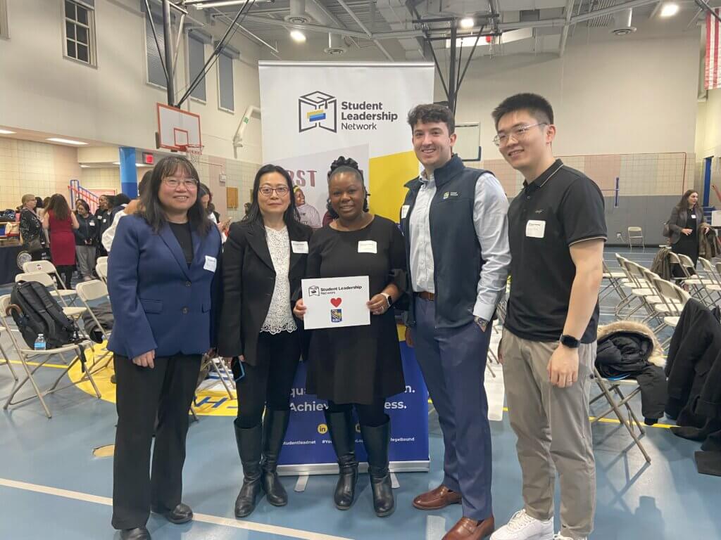 volunteers hold up RBC sign by Student Leadership Network banner