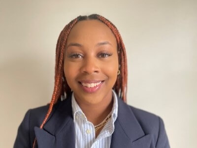Professionally dressed young Black woman with red braids in a dark grey suit jacket