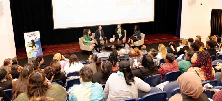 Four educators are seated on stage for panel discussion