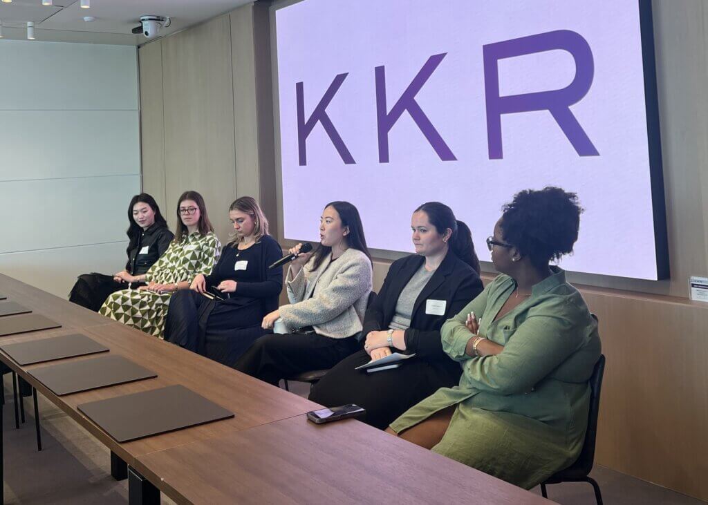 Six women sit on a panel in front of a boardroom