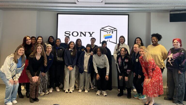 A group of people pose and smile in front of a screen displaying the Sony logo and a stylized cube icon with blue and yellow accents, celebrating the SUNY McConney EOP award.