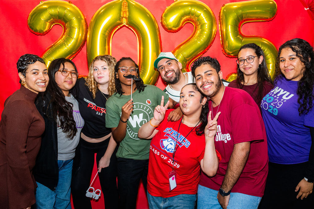 A group of students poses in front of large gold “2025” balloons and a red background, smiling and making peace signs.