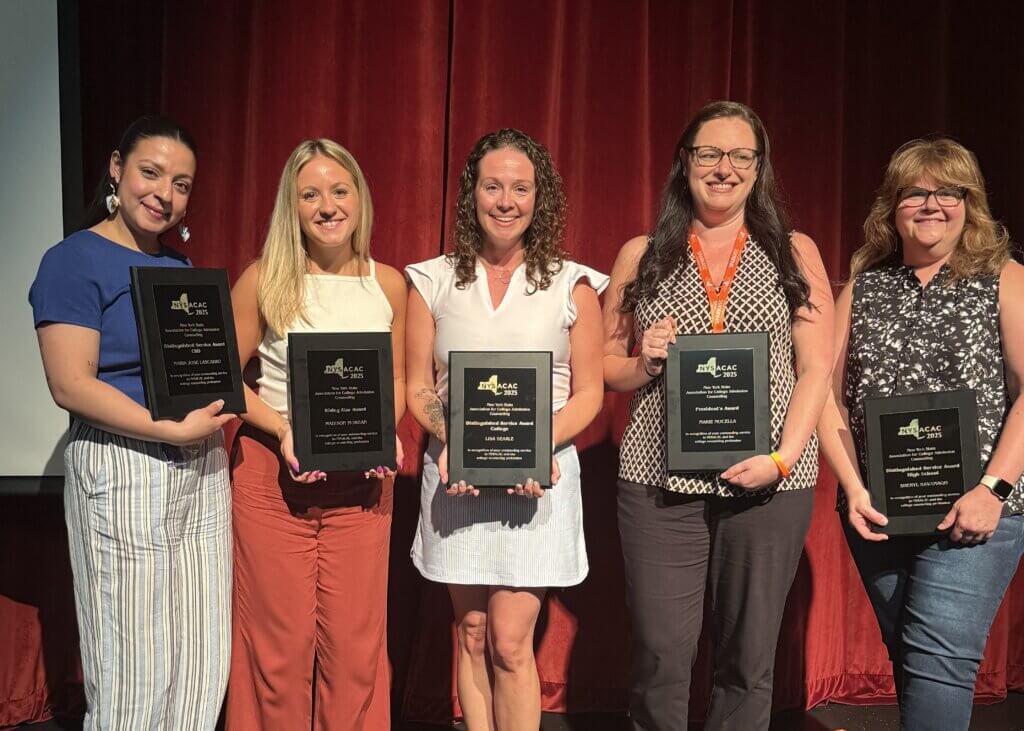 Five women stand in front of a red curtain, each holding a black plaque award at the NYSACAC conference.