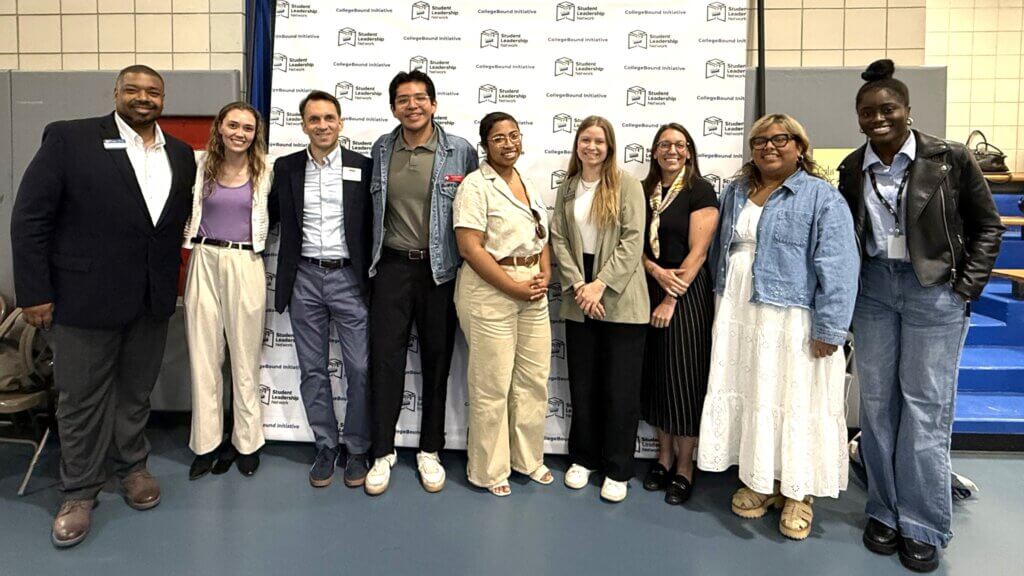 Nine people from colleges that partner with QuestBridge and Posse Foundation programs stand inside a school for a scholarship event