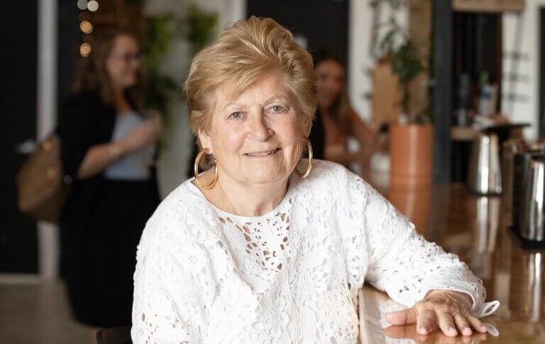 Older woman with short blonde hair and hoop earrings sits at a table