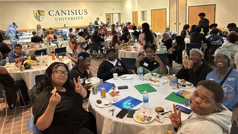 A large group of students sit at round tables eating and socializing at Canisius University as part of college persistence programs