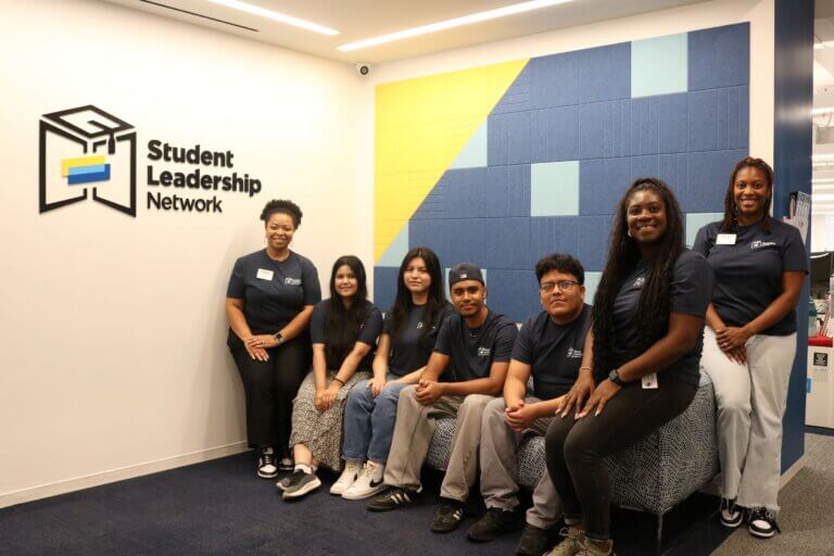 Seven students and staff wearing matching navy t-shirts pose for a photo, with a Student Leadership Network sign on the wall.