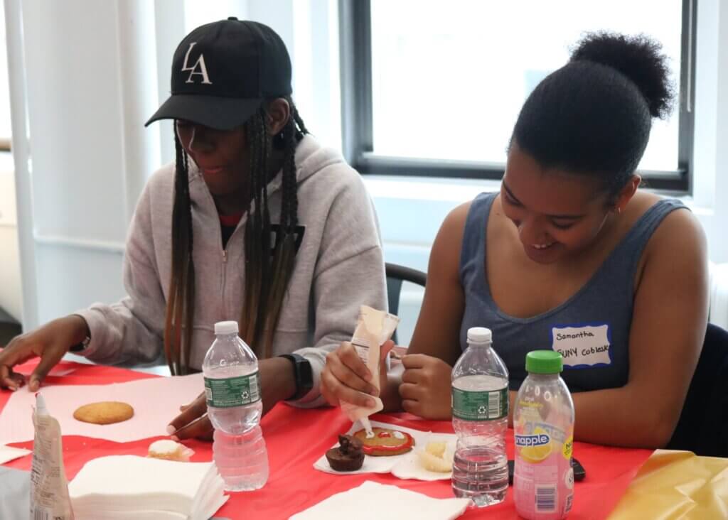 Two people sit at a table decorating cookies with icing.
