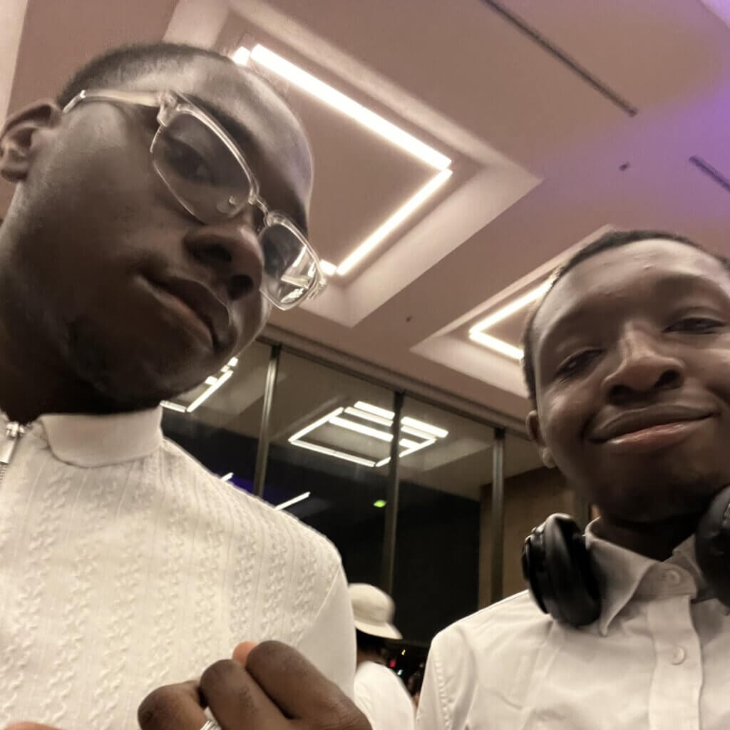 Two young men in white shirts pose for a selfie indoors under bright ceiling lights on Howard University campus