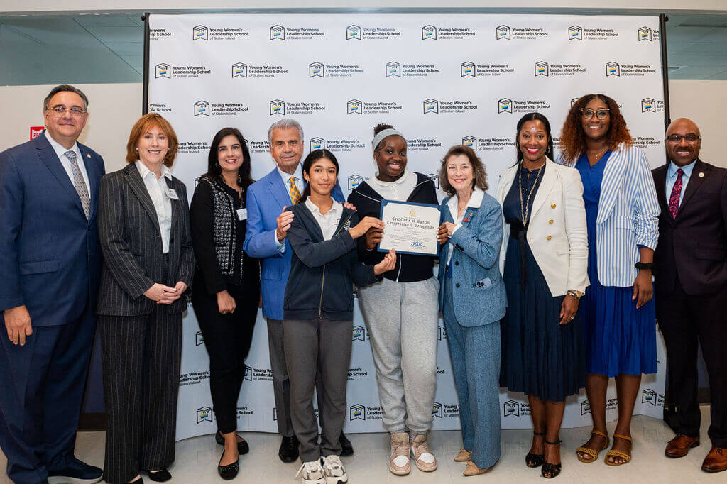 A group of community leaders and elected officials smile with students at TYWLS Staten Island