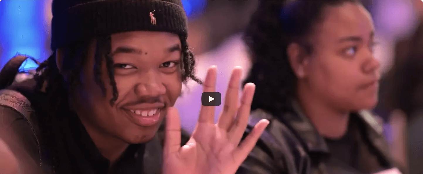 A student smiles and waves at the 2023 (Em)Power Breakfast event.