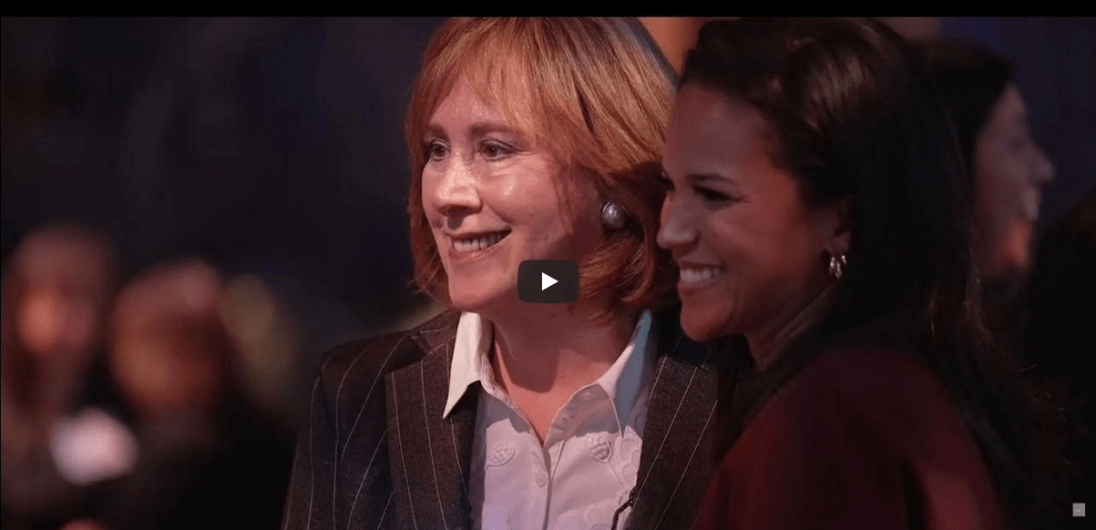 Ann Tisch, in a striped blazer and Laura Jarrett in a dark outfit, stand close together smiling at the 2024 Power Breakfast event.