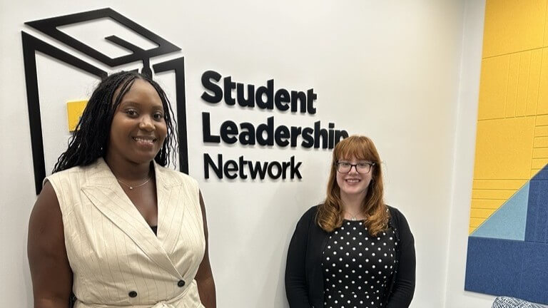 Two women stand in front of a wall with the sign Student Leadership Network