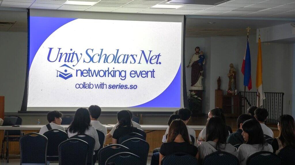 Attendees sit facing a large projected screen displaying Unity Scholars Net. networking event