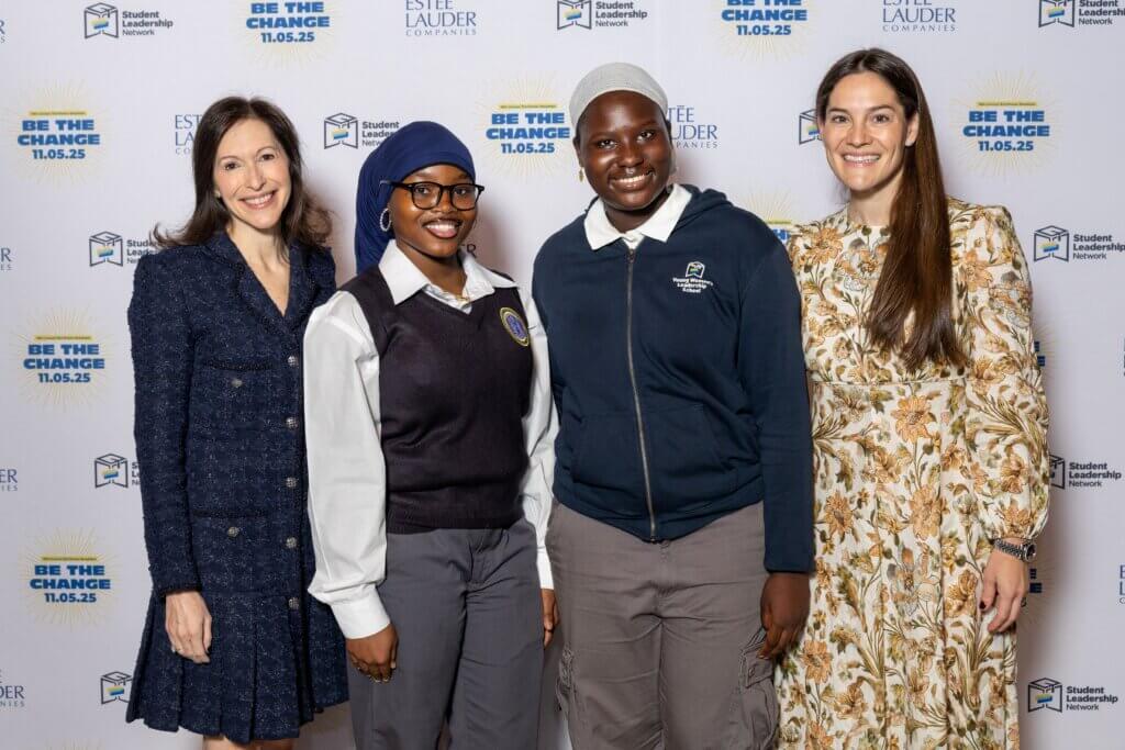 Two women and two students stand side by side, smiling, in front of a backdrop with logos and the text Be the Change 11.05.25 and Estée Lauder Companies.