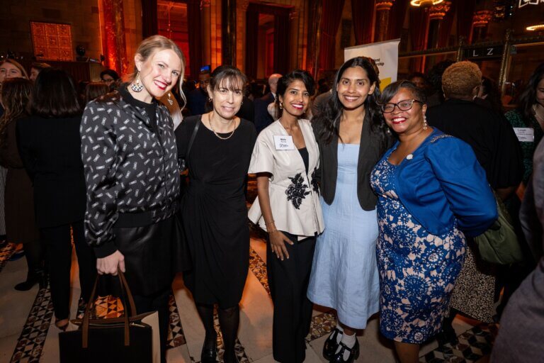 Five women in business attire stand together and smile for a group photo