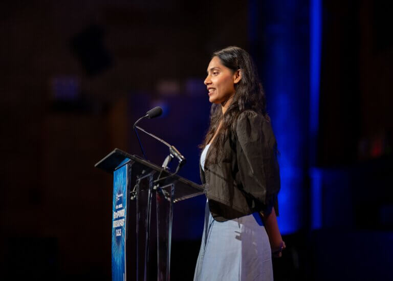 Farzana Hossain stands at a podium speaking into a microphone